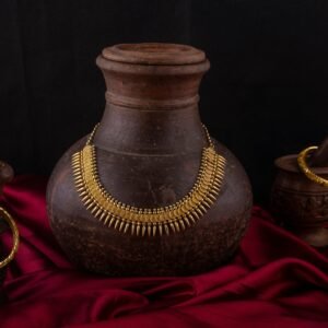 Elegant still life of traditional Indian necklace and bangles on vintage pottery with red fabric backdrop.