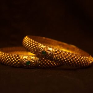 Luxurious gold bangles with intricate designs and emerald accents against a dark backdrop.